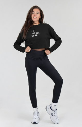 Woman wearing a black 'Le Pickle Club' sweatshirt and leggings on a white background