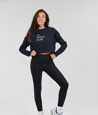 Woman wearing a black 'Le Pickle Club' sweatshirt and leggings on a white background
