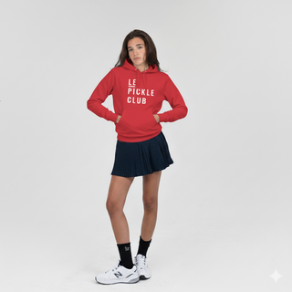 Person wearing a red 'LE PICKLE CLUB' hoodie and navy pleated skirt on a white background