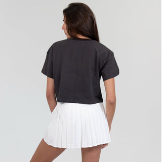 Woman wearing a black t-shirt and white pleated skirt on a plain background