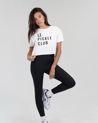 Woman wearing a white 'Le Pickle Club' t-shirt and black leggings on a gray background