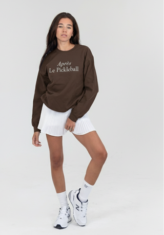 Person wearing a brown sweatshirt with text and white shorts on a light gray background