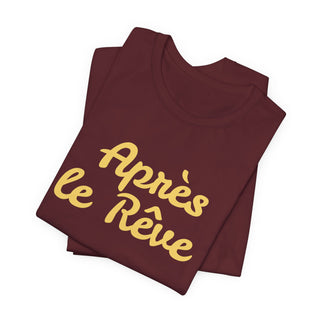 Folded maroon t-shirt with yellow text 'Après le Rève' on a white background