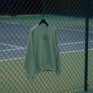 Green sweatshirt with a logo on a hanger against a tennis court fence.