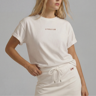 Woman wearing a white 'Le Petite Club' t-shirt and skirt on a gray background
