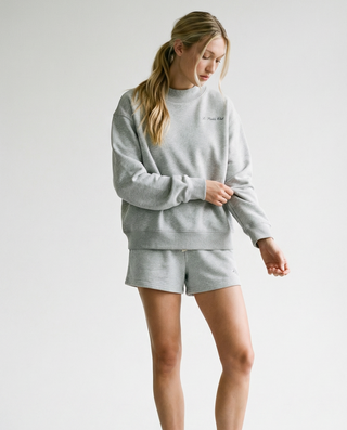 Person wearing a gray sweatshirt and shorts set with white sneakers on a plain background