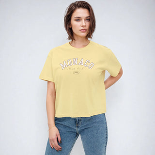 Woman wearing a yellow t-shirt with 'Monaco' print against a plain background