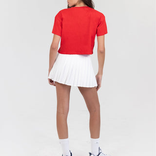 Person wearing a red crop top and white pleated skirt on a white background