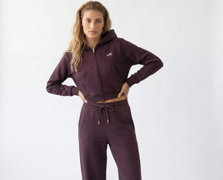 Woman wearing a maroon tracksuit with a logo on a white background