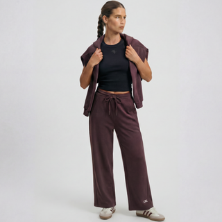 Woman wearing a black top and brown pants with a matching jacket on a white background