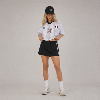 Person wearing a striped sports jersey, black skirt, and cap on a plain background