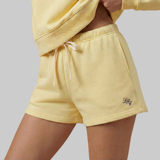 Person wearing a yellow loungewear set with a logo on a beige background
