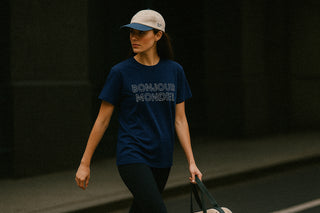 Woman wearing a bonjour mode, le pickle club, navy blue t-shirt with 'Bonjour Monde!' text, walking on a Parisian street.