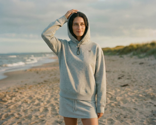 Person wearing a gray hoodie on a beach with ocean and sky in the background