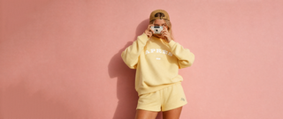 Person wearing a yellow outfit with 'LOVE' printed on it, standing against a pink background.
